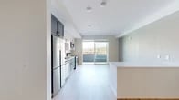 Located at 215 E State St in the heart of downtown Ithaca, NY, this modern studio offers a thoughtfully designed open-concept layout that maximizes every inch of its single-floor footprint. Light-toned hardwood-style flooring runs throughout, creating a cohesive and airy feel that enhances the sense of space.

The kitchen is a standout feature, showcasing a two-tone design with slate-gray lower cabinets and crisp white upper cabinetry, all fitted with brushed nickel hardware. Stainless steel appliances — including a full-size refrigerator, dishwasher, microwave, and range — complement the white quartz countertops and stainless steel sink. A peninsula with matching teal-blue cabinetry provides additional storage and serves as a natural divider between the kitchen and living area.

Large floor-to-ceiling sliding glass doors flood the living space with natural light and frame scenic views of the surrounding Ithaca landscape and hillside, lending the studio an elevated, open ambiance.

The bathroom is well-appointed with a gray vanity, white quartz countertop, an illuminated mirror, and a spacious glass-enclosed walk-in shower with brushed nickel fixtures. A dedicated closet and two hallway areas provide practical storage solutions. Clean white walls and recessed lighting throughout contribute to the studio's crisp, contemporary aesthetic.
