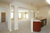 This single-floor residence offers a well-organized and functional layout designed for comfortable everyday living. The spacious living room is finished with plush wall-to-wall carpeting and crowned with elegant crown molding, centered around a tile-surround fireplace with a classic white mantel. Natural light filters in through a window nearby, enhancing the room's warm, neutral palette. The living area connects seamlessly to the kitchen via a breakfast bar peninsula, making the space ideal for both casual dining and entertaining. The galley-style kitchen is outfitted with rich, warm-toned wood cabinetry, generous counter space, and a full suite of stainless steel appliances including an electric range, over-the-range microwave, and refrigerator. Light wood-look flooring runs throughout the kitchen and wet areas, offering a clean, low-maintenance surface. The bedrooms are carpeted and well-proportioned, with at least one featuring a ceiling fan with light kit and a window allowing natural light. The bathrooms are finished with wood-toned vanity cabinetry and light tile flooring; one includes a soaking tub with tiled surround. A dedicated in-unit laundry area accommodates a stacked washer and dryer, adding everyday convenience to this thoughtfully designed residence.