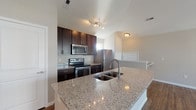 Located at 4890 Edwards Farm Rd. in Hilliard, Ohio, this single-floor residence offers a thoughtfully designed layout with contemporary finishes throughout. The kitchen serves as a central highlight, showcasing rich dark-espresso cabinetry, granite countertops, a large island with an undermount sink, and a full suite of stainless steel appliances including a refrigerator, electric range, and over-the-range microwave. Track lighting accents the kitchen's vaulted ceiling, adding warmth to the space. Hardwood-style flooring flows seamlessly through the kitchen and into the open living area, which benefits from generous natural light courtesy of large windows and French doors that lead to an outdoor space. The bedroom features plush carpeting and multiple windows that invite ample daylight, creating a comfortable and restful retreat. The bathroom is well-appointed with a granite-topped vanity with dark cabinetry, a combination tub and shower, and a window for natural ventilation. Neutral-toned walls throughout the unit provide a clean, versatile backdrop. The open-concept design between the kitchen and living area enhances the sense of space and promotes easy flow between functional areas, making this a practical and attractive residence in the Hilliard community.