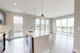 Located in Charlotte, NC, this contemporary 2-bedroom, 2-bathroom residence offers a thoughtfully designed open-concept layout finished with light wood-tone flooring and a neutral color palette throughout. The combined kitchen and living area serves as the heart of the home, anchored by a central island with a undermount sink, quartz countertops, and stainless steel appliances, including a dishwasher. Sleek, dark-toned cabinetry lines the kitchen walls, complemented by a clean tile backsplash. Dual pendant lights in brushed gold add a refined touch overhead. Floor-to-ceiling windows and a glass-panel balcony door bathe the living area in natural light while offering expansive views of the Charlotte skyline and surrounding cityscape. The bedrooms are well-proportioned, featuring the same warm hardwood-style flooring, ceiling fans, and soft neutral walls. The primary bathroom is appointed with a glass-enclosed walk-in shower tiled in classic white subway tile, a modern vanity with quartz countertops, and brushed nickel fixtures. The second bathroom mirrors this quality with a full soaking tub and shower combo, also finished in white subway tile. Clean lines, quality materials, and abundant natural light define the overall ambiance of this well-appointed Charlotte residence.