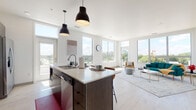 Located at 2518 Winnebago St in Madison, Wisconsin, this modern single-floor residence showcases a thoughtfully designed open-concept layout with clean architectural lines and contemporary finishes throughout. Light hardwood-style flooring flows seamlessly across the entire space, complementing the crisp white walls and creating a bright, cohesive aesthetic.

The kitchen serves as a central hub, featuring a large island with a white quartz countertop and seating for multiple bar stools, dark wood cabinetry with open shelving, a subway tile backsplash, a stainless steel appliance suite including a French door refrigerator and range, and a sleek ventilation hood. Dramatic black pendant lights anchor the space overhead. The kitchen opens directly into the living area, which is bathed in natural light from expansive floor-to-ceiling windows offering elevated views of the surrounding Madison neighborhood and greenery.

The bedrooms are generously proportioned, each featuring large windows that capture ample daylight and outdoor scenery. One bedroom includes a dedicated workspace with a built-in desk setup, while another features an open closet with built-in shelving. The bathroom is clean and modern, appointed with a glass-enclosed walk-in shower, a white vanity, and wood-tone flooring. Overall, the space delivers a refined, contemporary living environment with a bright and airy ambiance throughout.