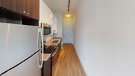 Located at 138 Atando Ave in Charlotte, NC, this single-floor unit offers a clean, modern aesthetic characterized by crisp white walls and warm wood-style flooring that flows consistently throughout the space. The open layout is anchored by a bright living area featuring a ceiling fan with integrated lighting, large sliding glass doors, and an adjacent window that together invite generous amounts of natural light, creating an airy and welcoming atmosphere.

The galley-style kitchen is efficiently designed, featuring dark cabinetry contrasted by white upper cabinets, granite countertops, and a full suite of stainless steel appliances including a refrigerator, microwave, electric range, and dishwasher. Track lighting overhead adds a contemporary touch and ensures excellent task illumination throughout the kitchen corridor.

A barn-style sliding door adds a distinctive architectural detail, providing both functional room separation and a modern design accent. The bathroom continues the refined aesthetic with a dark wood vanity topped with granite countertops, an undermount sink, and a large mirror framed by a lighted fixture above. The space is thoughtfully finished with consistent, neutral tones throughout, resulting in a cohesive and move-in ready environment.
