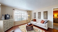 This 1-bedroom, 1-bathroom residence is efficiently laid out across a single floor, offering a comfortable and cohesive living environment. The living room serves as the heart of the home, featuring rich hardwood-style flooring, a textured ceiling, and multiple large windows dressed with sheer white curtains that flood the space with natural light. The open flow connects seamlessly to a dedicated dining area, which includes a ceiling fan and sliding glass door that provides access to an outdoor balcony. The kitchen is outfitted with white cabinetry, a full-size refrigerator, and an electric range, offering practical functionality. The bedroom is a spacious retreat with plush carpeting, a ceiling fan with light fixture, and windows allowing ample natural light. A bold accent wall adds a warm, inviting character to the room. The bedroom is complemented by a walk-in closet featuring built-in shelving for generous storage. The full bathroom includes a tub-shower combination with tile surround, hardwood-style flooring, and a vanity with stone-look countertops. A dedicated entrance completes the layout, making this a well-rounded and functional single-level residence.