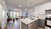 Located at 3355 Club Dr in Lawrenceville, GA, this thoughtfully designed single-floor residence combines modern aesthetics with functional living. The open-concept layout seamlessly connects the kitchen and living area, creating an inviting and cohesive space. The kitchen is a standout feature, showcasing granite countertops, a central island with bar seating, two-tone cabinetry with white uppers and gray lowers, a classic subway tile backsplash, and a full suite of stainless steel appliances including a side-by-side refrigerator, range, and microwave. Pendant lighting over the island adds a contemporary touch. The living area is warm and welcoming, featuring wood-look flooring, a woven pendant light fixture, large windows with exterior views, and French-style doors that invite natural light. The bedrooms offer plush carpeting and generous windows, with one bedroom highlighted by a distinctive white brick accent wall. The bathroom is clean and bright, finished with white subway tile surrounding a full tub-shower combination and wood-look flooring. Throughout the space, textured accent walls and consistent, neutral tones create a cohesive and polished ambiance ideal for modern living.