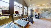 Located at 1000 Artistry Dr in Midlothian, Virginia, this single-floor fitness center is a thoughtfully designed recreational amenity offering a comprehensive workout experience. The space is divided into several distinct zones, each tailored to a specific type of training.

The main exercise area features soaring vaulted ceilings, large windows that flood the room with natural light, and views of the surrounding community. It is equipped with a full suite of cardio machines — including treadmills, ellipticals, and a recumbent bike — alongside a multi-station strength training system and a dedicated free weights area with a dumbbell rack and adjustable bench. Wall-mounted televisions and ceiling fans enhance comfort during workouts. A large-scale abstract mural serves as a dramatic artistic backdrop to the strength equipment.

A separate functional training room houses an Outrace multi-purpose rig complete with a heavy bag, battle ropes, climbing ladder, and cable attachments, ideal for high-intensity and cross-training workouts.

An open studio space with vaulted ceilings, mirrors, and soft flooring provides a versatile area for stretching, yoga, or group fitness. Colorful abstract artwork adorns the walls, contributing to an energizing ambiance.

A refreshment station near the entrance features a water fountain, bottle-filling station, a small prep counter, and a mini-refrigerator, framed by a striking geometric patterned tile accent wall with gold, black, and white tones.