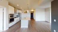 Located at 1455 W Lake St in Minneapolis, MN, this single-floor residence offers a thoughtfully designed layout with modern finishes throughout. The kitchen serves as a central highlight, featuring white shaker cabinetry, a striking tile backsplash, stainless steel appliances including a gas cooktop and double wall ovens, and a large center island with a quartz countertop and undermount sink. Globe pendant lights in brushed gold add a contemporary touch above the island. The open-plan living area extends naturally from the kitchen and includes a fireplace, with rich hardwood-style flooring throughout the main living spaces. Large windows and a sliding glass door allow abundant natural light and offer elevated views of the Minneapolis skyline and surrounding neighborhood. The bedrooms are finished with plush carpeting and feature generous walk-in closets equipped with wire shelving systems. The bathrooms are clean and modern, appointed with white cabinetry, vessel-style sinks, large mirrors, and light tile flooring. One bathroom includes a soaking tub surrounded by classic white subway tile, while the other offers a tiled walk-in shower. The overall aesthetic is cohesive and contemporary, combining neutral tones with modern fixtures for a refined, move-in-ready living environment.