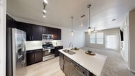Located at 2323 Wolf Ranch Pkwy in Georgetown, TX, this one-bedroom, one-bathroom unit offers a well-designed single-floor layout that makes efficient use of its cozy footprint. The open-concept kitchen and living area serves as the heart of the home, featuring rich dark cabinetry, white subway tile backsplash, stainless steel appliances including a gas range, built-in microwave, and French door refrigerator. A central kitchen island with a white quartz countertop and undermount sink is illuminated by stylish pendant lights, creating an ideal space for both meal prep and casual dining. Light wood-style flooring flows through the kitchen, transitioning to plush carpet in the living area, which is anchored by a sleek linear electric fireplace and ceiling fan. Natural light fills the space through multiple windows with blinds. The bedroom is a comfortable retreat with carpet flooring, a ceiling fan, and generous natural light. The walk-in closet offers multi-tier shelving and hanging rods for ample storage. The bathroom features a dual-sink vanity with dark cabinetry and white countertops, tile flooring, a large mirror, and a shower-tub combination.
