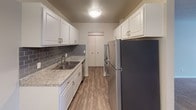 Located at 1919 Silver Bell Rd in Eagan, Minnesota, this single-floor residence offers a thoughtfully designed layout with a range of updated finishes and functional spaces. The galley-style kitchen is a standout feature, showcasing white shaker cabinetry with brushed nickel hardware, granite-look countertops, a gray subway tile backsplash, stainless steel appliances, and durable wood-look flooring — creating a clean, modern aesthetic. Adjacent to the kitchen, the open living and dining areas offer a smooth transition between spaces, with warm carpet in the living room and wood-look flooring in the dining area, illuminated by a pendant light fixture. The bedroom is generously sized with plush carpeting, a window with natural light, a wall-mounted AC unit, and baseboard heating. A spacious walk-in closet with wire shelving provides ample storage. The primary bathroom features a tub-shower combination with white tile surround and mosaic tile flooring, while a separate vanity area includes a wide mirror and white cabinetry. A private water closet with tile flooring adds an extra layer of convenience. Throughout the unit, neutral tones and clean lines create a bright, move-in-ready atmosphere.