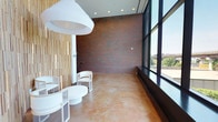 This single-floor space showcases a thoughtfully curated blend of industrial and modern design elements. Exposed red brick walls serve as a striking architectural focal point, adding texture and warmth throughout the interior. The polished concrete flooring provides a smooth, durable foundation that complements the raw character of the brickwork, creating a refined industrial aesthetic.

Floor-to-ceiling windows line one side of the space, flooding the interior with abundant natural light and offering open views of the surrounding outdoor environment. The expansive glazing creates a seamless connection between the interior and the outside world, enhancing the overall sense of openness and airiness.

A vertical wood slat accent wall introduces a layer of organic warmth, serving as an elegant contrast to the harder surfaces of brick and concrete. The space is furnished with sleek, white modern seating — including rounded chairs and a low circular table — that reinforces a clean, minimalist sensibility. A large, sculptural pendant light hangs overhead, adding a bold design statement while contributing to the welcoming ambiance.

The combination of natural materials, generous daylighting, and carefully selected furnishings gives this space a sophisticated yet approachable character, well-suited for a lounge, reception, or collaborative gathering area.