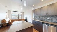 Located at 1028 N Hamilton St in Spokane, WA, this modern 3-bedroom, 3-bathroom unit offers a well-designed, single-floor layout with contemporary finishes throughout. The open-concept kitchen serves as the heart of the home, featuring dark espresso cabinetry, a stone-topped center island, a mosaic tile backsplash, stainless steel appliances including a full-size refrigerator and dishwasher, and stylish pendant lighting. The kitchen flows seamlessly into the living area, which benefits from expansive windows that frame elevated city views and flood the space with natural light. Hardwood-style flooring runs throughout the unit, adding warmth and continuity. Each of the three bedrooms is well-proportioned, with the primary bedroom offering a spacious walk-in closet equipped with wire shelving and wood flooring. The bedrooms feature large windows with views of the surrounding Spokane skyline. Three full bathrooms are finished with stone-toned tile flooring, dark wood vanities with stone countertops, and tub-shower combinations with brushed nickel fixtures. A dedicated laundry room houses a stacked washer and dryer alongside the HVAC system. Two hallways provide efficient circulation throughout the unit, making the layout both practical and functional.