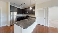 This single-floor residence offers a thoughtfully designed layout with a cohesive blend of modern finishes and functional living spaces. The kitchen serves as a standout centerpiece, showcasing dark espresso cabinetry, granite countertops, a classic white subway tile backsplash, and a full suite of stainless steel appliances including a refrigerator, electric range, and built-in microwave. A curved kitchen island with pendant lighting provides additional prep space and a casual gathering area, while rich hardwood flooring anchors the space with warmth. The bedrooms are finished with plush wall-to-wall carpeting and feature windows fitted with horizontal blinds that invite natural light. One bedroom connects directly to a walk-in closet with built-in wire shelving, offering generous storage capacity. The primary bathroom features a dark vanity with granite countertops, a large mirror with vanity lighting, and light tile flooring. A second full bathroom includes a soaking tub with full tile surround and recessed lighting. Throughout the residence, neutral wall tones, clean white trim, and consistent flooring choices create a calm, cohesive aesthetic that is both inviting and move-in ready.