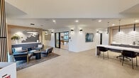 Located at 6021 Lakewood Dr W in University Place, WA, this thoughtfully designed single-floor community amenity facility offers a comprehensive range of spaces for residents to gather, relax, and stay active. The welcoming lobby greets visitors with large-format stone-look tile flooring, recessed and wall-mounted lighting, curated artwork, and a sleek reception counter — setting a polished, modern tone throughout.

The open lounge area flows seamlessly into a dedicated game room, which features a full-size pool table, shuffleboard table, and additional game surfaces beneath a striking slatted wood ceiling detail and modern pendant lighting. Sliding glass doors connect this space directly to an outdoor terrace, flooding the interior with natural light.

A standout great room showcases a dramatic floor-to-ceiling wood-clad fireplace wall with a mounted display, flanked by expansive black-framed glass walls and sliding doors that open to the outdoors, creating a bright and airy atmosphere.

The well-equipped fitness center is lined with large windows overlooking lush greenery, housing both strength and cardio equipment. Additional spaces include a private office area with a textured 3D tile accent wall, custom cabinetry, and materials display, as well as a utility/storage room. A connecting hallway ties all areas together, ensuring smooth circulation throughout this versatile and amenity-rich facility.