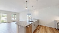 Located at 1471 Route 9 in Halfmoon, NY, this well-appointed one-bedroom, one-bathroom unit offers a thoughtfully designed layout across a single floor. The open-concept living and kitchen area forms the heart of the space, where light hardwood flooring, white walls, and abundant natural light from multiple windows create a bright, airy atmosphere. The kitchen is a standout feature, equipped with stainless steel appliances including a refrigerator, microwave, and dishwasher, complemented by grey shaker-style cabinetry, granite countertops, and a large center island with a built-in sink. Stylish pendant lighting above the island adds a contemporary touch. The living area flows seamlessly from the kitchen, offering generous room for entertaining. The bedroom is carpeted for comfort, features a natural window view, and connects to a walk-in closet outfitted with wire shelving for ample storage. The bathroom maintains the unit's clean aesthetic with light hardwood flooring, grey cabinetry with granite countertops, and assist bars. Additional access to an outdoor area is provided via a sliding glass door off the living space, enhancing the unit's connection to the outdoors.