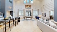 Located at 442 Robert Smalls Pkwy in Beaufort, South Carolina, this single-floor community space offers a generously sized, open-concept layout designed for both socializing and relaxation. The interior is immediately distinguished by its dramatically tall ceilings, which amplify the sense of openness and allow abundant natural light to pour in through large windows and transom glass above the main entrance.

The flooring throughout is a light-toned herringbone hardwood pattern, lending warmth and visual interest to the expansive layout. A statement chandelier anchors the central gathering area, which features a billiards table, plush lounge seating in neutral tones accented by navy blue upholstery, and layered area rugs. Sliding barn-style doors with frosted glass panels divide zones while maintaining an airy, connected feel.

One wall is dressed in bold botanical wallcovering in blue and grey tones, framing a built-in counter with a coffee and beverage station. A cozy nook with built-in bench seating provides an intimate retreat within the larger space. A textured blue accent wall with a wall-mounted television creates a distinct media lounge area. The entrance corridor leads seamlessly into the main floor, completing a cohesive, well-appointed interior.