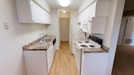 This single-floor, one-bedroom, one-bathroom residence offers a practical and comfortable layout designed to maximize its well-proportioned footprint. Neutral gray walls and warm beige carpeting flow through the living area and bedroom corridor, creating a cohesive and inviting atmosphere. The open passage connecting the living space to the bedroom provides a sense of depth, with white bi-fold closet doors adding clean contrast along the hallway.

The galley-style kitchen is efficiently designed, featuring white cabinetry with ample upper and lower storage, granite-look countertops, a stainless steel sink, and white appliances including a range, dishwasher, refrigerator, and over-the-range microwave. Light wood-look flooring runs through the kitchen and into the adjacent dining area, which benefits from a dedicated overhead light fixture and a window that brings in natural light.

The bathroom is well-equipped with a granite-topped vanity, white cabinetry, a large mirror with a medicine cabinet, and a shower/tub combination with chrome fixtures and towel bars. Wood-look flooring continues in the bathroom, complementing the warm, neutral palette carried throughout the entire space.