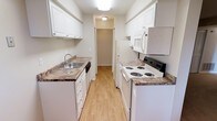 This single-floor, one-bedroom, one-bathroom residence offers a practical and comfortable layout designed to maximize its well-proportioned footprint. Neutral gray walls and warm beige carpeting flow through the living area and bedroom corridor, creating a cohesive and inviting atmosphere. The open passage connecting the living space to the bedroom provides a sense of depth, with white bi-fold closet doors adding clean contrast along the hallway.

The galley-style kitchen is efficiently designed, featuring white cabinetry with ample upper and lower storage, granite-look countertops, a stainless steel sink, and white appliances including a range, dishwasher, refrigerator, and over-the-range microwave. Light wood-look flooring runs through the kitchen and into the adjacent dining area, which benefits from a dedicated overhead light fixture and a window that brings in natural light.

The bathroom is well-equipped with a granite-topped vanity, white cabinetry, a large mirror with a medicine cabinet, and a shower/tub combination with chrome fixtures and towel bars. Wood-look flooring continues in the bathroom, complementing the warm, neutral palette carried throughout the entire space.