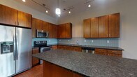 Located on North High Street in Columbus, Ohio's vibrant Short North neighborhood, this single-floor residence offers a thoughtfully designed layout with contemporary finishes throughout. The open-concept kitchen serves as a centerpiece, showcasing warm-toned wood cabinetry extending to the ceiling, dark granite countertops, a large central island, light blue glass tile backsplash, and a full suite of stainless steel appliances including a refrigerator with ice maker, range, microwave, and dishwasher. Track lighting illuminates the kitchen from above, highlighting the rich hardwood-style flooring that flows seamlessly into the spacious living area. The living space is bathed in natural light from large windows with views of the surrounding neighborhood, creating an open and airy atmosphere. The bedroom features plush carpeting and its own windows for additional natural light. The bathroom is finished with neutral tile flooring, a dark vanity with granite countertop, and a large mirror. A dedicated in-unit laundry area with a full-size washer and dryer adds everyday convenience. Clean lines, neutral wall tones, and quality finishes define the overall modern aesthetic of this well-appointed urban residence.