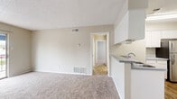 This 2-bedroom, 2-bathroom residence is laid out entirely on a single floor, offering a practical and efficient use of space throughout. The living area features neutral-toned carpet, a textured ceiling, and a sliding glass door that opens to a balcony, allowing natural light and outdoor views to flow into the room. Adjacent to the living space, the kitchen is equipped with wood-look flooring, white cabinetry, a stainless steel refrigerator, an electric range, built-in open shelving for additional storage, and an overhead range hood. The primary bedroom provides a comfortable retreat with plush carpet, a ceiling fan with light fixture, a window with blinds for natural light, and a spacious dual-panel closet offering generous storage. The primary bathroom features dual vanities with ample counter space, white cabinetry, wood-look flooring, and a private water closet. The second bathroom includes a full tub-shower combination and wood-look flooring. The second bedroom also features carpet and a ceiling fan. A hallway connects the private areas of the home, completing this well-organized and cohesive floor plan.