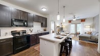 Located at 2300 Bluff Oak Way in Tallahassee, FL, this single-story, 2-bedroom, 2-bathroom residence offers a thoughtfully designed layout with a seamless open-concept living, dining, and kitchen area. The kitchen is a standout feature, showcasing rich dark cabinetry, light countertops, a white subway tile backsplash, and a suite of black appliances including a range, microwave, dishwasher, and refrigerator. A spacious kitchen island with pendant lighting provides additional seating and workspace, flowing naturally into the dining and living areas. Wood-look flooring runs throughout the main living spaces, complemented by ceiling fans for year-round comfort. The living room benefits from natural light through large windows. Both bedrooms are generously sized, featuring plush carpet flooring and ceiling fans. The primary bedroom connects to an en-suite bathroom with dark vanity cabinetry and wood-look flooring. The second bathroom mirrors the design aesthetic and includes a tub/shower combination. The residence also features a dedicated laundry area, a hallway connecting the spaces, and an impressive six closets, ensuring exceptional storage throughout. The overall ambiance is modern and cohesive, with a neutral palette accented by warm, rich tones.