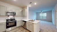 Located at 4225 East West Connector in Smyrna, Georgia, this single-floor residence offers a clean, modern aesthetic throughout. The open-concept kitchen flows seamlessly into the living area, creating a connected and functional layout. The kitchen is outfitted with gray shaker-style cabinetry, white countertops, and a full suite of stainless steel appliances including a refrigerator, range, over-the-range microwave, and dishwasher. A peninsula with an integrated sink adds additional prep space and serves as a natural divider between the kitchen and living area. Wood-look flooring runs throughout the kitchen and entry areas, while plush carpeting covers the living room and bedrooms. The living area is bright and inviting, featuring a ceiling fan and a window that overlooks an outdoor balcony. The bedrooms are comfortably sized, each with carpet flooring, neutral tones, and windows that allow ample natural light. The bathroom is finished with a gray vanity, white countertop, subway tile shower surround, and wood-look flooring, maintaining the consistent, contemporary style found throughout the home. Recessed lighting and ceiling fans contribute to a comfortable and well-lit living environment overall.