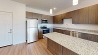 This well-designed single-floor unit offers two bedrooms and one bathroom across a efficiently utilized footprint. The open-concept kitchen and living area serves as the heart of the space, featuring rich dark-toned cabinetry, granite countertops, and a central island with additional seating and storage. Stainless steel appliances, including a refrigerator, range, and dishwasher, complement the contemporary aesthetic, while pendant lighting adds a polished finish. Light wood-style flooring runs throughout the main living areas, enhancing the sense of openness, and a large window in the living area invites natural light and outdoor views.

The hallway connects the living space to the bedrooms and bathroom, maintaining a clean, organized flow. The primary bedroom is a comfortable size, featuring carpeted flooring and access to a dedicated closet. The second bedroom also offers carpet, a ceiling fan, and a window with natural light. Both bedrooms share access to the full bathroom, which includes a granite-topped vanity, light wood cabinetry, and a tub-shower combination. Two closets throughout the unit provide practical storage solutions. The overall aesthetic is clean, modern, and neutral.