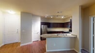 This single-floor residence offers a thoughtfully designed layout with a seamless flow between living and kitchen areas. The kitchen serves as a central highlight, featuring dark espresso cabinetry that extends to the ceiling, granite countertops, and a full suite of stainless steel appliances including a refrigerator, microwave, and range. A curved peninsula with a built-in sink provides additional workspace and casual dining space, while track lighting overhead ensures excellent task illumination. Hardwood-style flooring runs throughout the kitchen and entryway, creating a warm, cohesive look.

The open-concept design allows the kitchen to connect naturally to the carpeted living area, which offers generous space and access to additional rooms via a well-defined entry corridor with white panel doors. The bedrooms are carpeted and receive natural light through multiple windows fitted with horizontal blinds; one bedroom includes a ceiling fan for added comfort.

The bathroom features a wide vanity with dark cabinetry, a full-width mirror, tile tub-shower surround with decorative accent stripe, and tile flooring. An adjacent walk-in closet is outfitted with multiple wire shelving units, providing ample and organized storage. Neutral warm tones are used throughout, contributing to a consistent and inviting ambiance.