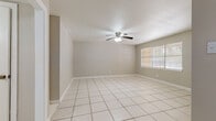 This single-story space features a straightforward, functional layout highlighted by light-toned ceramic tile flooring that runs consistently throughout the interior. The main living area is spacious and open, with neutral gray walls, white baseboards, and a ceiling fan with an integrated light fixture providing both airflow and overhead illumination. A window along one wall allows natural light to filter into the room, contributing to a bright and airy atmosphere. An adjacent area extends the usable living space, connected by an open passage and illuminated by a flush-mount ceiling light.

The galley-style kitchen is efficiently designed, featuring warm wood cabinetry along both sides, granite countertops, a stainless steel sink, and white appliances including a range and refrigerator. A window above the counter brings in additional natural light. The kitchen also includes a built-in utility panel on the wall.

The bathroom is finished with light tile flooring and includes a walk-in shower fully tiled in a warm beige stone-look tile with a built-in niche. Dark espresso-toned cabinetry supports a light countertop vanity, completing the space with a clean, neutral aesthetic throughout.