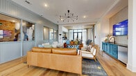 Located at 423 E 36th Street in Charlotte, NC, this thoughtfully designed single-floor communal space blends contemporary style with warm, inviting elements. Wide-plank hardwood flooring runs throughout, unifying the open-concept layout and lending a clean, cohesive aesthetic.

The main lounge area is generously proportioned, furnished with tan leather sofas, plush armchairs, and layered rugs beneath a striking sputnik chandelier. Multiple seating arrangements accommodate both casual socializing and relaxed gatherings. A statement sputnik-style pendant light anchors the central lounge, while recessed lighting provides even illumination throughout.

A dedicated wet bar area features a dramatic mosaic tile accent wall, dark countertops, bar seating with wood spindle-back stools, and stainless steel appliances — an ideal spot for entertaining. Adjacent to the bar is a glazed-partition private room with exposed brick walls and a large display screen, suitable for meetings or presentations.

Floor-to-ceiling black-framed windows flood the dining and lounge areas with abundant natural light and offer views of the surrounding Charlotte streetscape. A dining area with a dark table and mixed seating sits near these expansive windows, creating a bright and airy atmosphere. Elevator access is also present, highlighting the space's accessibility and functionality. The overall ambiance is modern yet approachable, balancing design-forward details with comfortable, livable warmth.