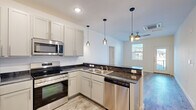 This single-story, 4-bedroom, 2-bathroom unit offers a thoughtfully laid-out floor plan designed for comfortable everyday living. The open-concept kitchen serves as the heart of the home, showcasing crisp white shaker cabinetry, dark granite-style countertops, a peninsula with pendant lighting overhead, and a full suite of stainless steel appliances including a refrigerator, electric range, microwave, and dishwasher. Wood-look plank flooring flows seamlessly through the kitchen and living areas, lending a clean, contemporary feel. The living room is bright and welcoming, featuring a ceiling fan, a glass-panel entry door, and a window that brings in natural light. The four bedrooms offer a quieter retreat, with soft carpet underfoot and windows fitted with blinds. The primary bedroom provides a comfortable and private space. Two well-appointed bathrooms mirror the home's consistent design language, featuring granite-topped vanities with undermount sinks, white cabinetry, and wood-look tile flooring. One bathroom includes a full tub-shower combination. Two closets and two kitchen areas round out the functional layout, making this unit highly practical for shared or multi-occupant living arrangements.