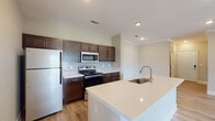 Located at 195 N Creek Dr in Summerville, SC, this single-floor residence offers a thoughtfully designed open-concept layout that seamlessly connects the kitchen, dining, and living areas. The kitchen serves as the centerpiece of the home, featuring rich dark-espresso cabinetry, light quartz countertops, a classic subway tile backsplash, and a full suite of stainless steel appliances including a refrigerator, range, and microwave. A generous kitchen island with an integrated sink adds both functional workspace and a natural gathering point that opens directly to the living area. Light wood-look flooring runs throughout the main living spaces, complementing the neutral warm-beige walls and white trim for a clean, modern aesthetic. Crown molding accents the dining area, adding a refined touch. The bedrooms are carpeted and filled with natural light through large windows with views of the surrounding greenery. Two bathrooms mirror the home's design language, featuring dark wood vanities, white quartz countertops, framed mirrors, and wood-look tile flooring; one includes a tub-shower combination. The overall ambiance is bright, neutral, and move-in ready, making this Summerville home a practical and comfortable living space.