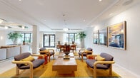 The Pool House at 1101 Kingsley St in Asbury Park, NJ is a thoughtfully designed amenity space that seamlessly blends comfort, style, and function across a single, generously proportioned floor. The open layout is anchored by multiple distinct zones that flow naturally into one another, creating an inviting and social atmosphere throughout.

The main lounge area features retro-modern seating with warm wood-framed chairs upholstered in muted purple tones, accented by bold mustard-yellow area rugs with graphic striped borders. A sculptural tiled coffee table serves as a centerpiece, complemented by colorful side tables in orange and red lacquer. A separate seating zone offers neutral-toned sofas and sleek accent chairs arranged around another tiled coffee table, ideal for relaxed conversation.

A standout feature is the full-width built-in media wall finished in powder blue, housing a large flat-screen television flanked by open shelving with curated décor. Above, a distinctive tray ceiling with circular cutouts and globe pendant lighting adds architectural drama.

The dining area accommodates a large round table surrounded by mid-century modern chairs, positioned near floor-to-ceiling windows and glass double doors that flood the space with natural light and provide views of the outdoors. Framed artwork throughout adds a gallery-like quality, while lush indoor plants introduce a refreshing natural element to this polished, resort-inspired gathering space.