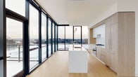 This contemporary two-floor residence offers a refined living experience defined by clean lines, high-end finishes, and sweeping panoramic views. The main living level is anchored by an expansive open-plan kitchen and living area, where floor-to-ceiling glass walls flood the space with natural light and frame dramatic cityscape views. The chef's kitchen is outfitted with light wood cabinetry, a gas cooktop, stainless steel appliances, and a sleek white waterfall island with an integrated sink — all beneath modern pendant lighting. Light hardwood flooring runs throughout, reinforcing the warm, minimalist aesthetic. A sculptural curved staircase with a dark steel frame and horizontal cable railings serves as a striking architectural centerpiece, connecting the two levels with both function and artistry. The upper floor hosts three well-proportioned bedrooms, each featuring large windows with elevated city views. The primary bedroom offers a generous footprint with corner glass walls maximizing natural light. The three bathrooms are finished with large-format neutral tiles, floating vanities, backlit mirrors, and glass-enclosed showers, with one bathroom also featuring a soaking tub. A dedicated closet with built-in shelving and hanging rods provides practical storage. The overall ambiance is modern and light-filled throughout.