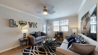 This single-floor residence offers a thoughtfully designed layout that balances comfort and functionality. The living room serves as the heart of the home, featuring crown molding, hardwood-style flooring, and a ceiling fan with integrated lighting. Multiple windows fitted with blinds allow natural light to fill the space, while a bold black-and-white patterned area rug and contemporary furnishings contribute to its modern aesthetic.

The kitchen is well-equipped and visually striking, showcasing rich dark-espresso cabinetry that extends to the upper walls, granite-look countertops, and a full suite of black appliances including a refrigerator, electric range, and over-the-range microwave. Light wood-style flooring ties the space together and complements the cabinetry's warm tones.

Both bathrooms follow a consistent design language, each featuring dark vanity cabinetry, granite-look countertops, a large mirror, tiled tub-shower combinations, and light stone-look tile flooring, lending a clean, polished finish.

The bedrooms are carpeted for comfort and include natural light from windows with blinds and curtains. Each room offers adequate space for full bedroom furniture arrangements, maintaining the residence's cohesive, contemporary style throughout.