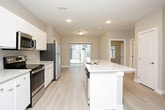 This single-floor unit offers a well-designed, contemporary layout with a cohesive neutral color palette and clean finishes throughout. The open-concept kitchen serves as a central hub, featuring white cabinetry, granite-style countertops, stainless steel appliances including a range, microwave, and refrigerator, and a center island with a built-in sink. Light wood-style luxury vinyl flooring runs through the kitchen and main living areas, contributing to a bright, airy feel. Recessed lighting and sliding door access to an outdoor area further enhance the kitchen and living space.

The bedrooms are carpeted and finished with soft gray walls and white trim. One bedroom includes a closet and direct access to a private en-suite bathroom, which features a dual-sink vanity with granite-style countertops and white cabinetry. A secondary full bathroom offers a single-sink vanity with matching finishes and a tub-shower combination. A dedicated laundry area accommodates a full-sized washer and dryer with additional wire shelving for storage. The overall design is modern and functional, presenting a move-in ready space with consistent, contemporary finishes from room to room.