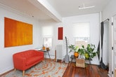 This single-floor residence offers a well-organized layout that makes efficient use of its footprint, with warm hardwood flooring flowing throughout the main living spaces. The kitchen is outfitted with sleek white cabinetry, stone-look countertops, and stainless steel appliances including a gas range, dishwasher, and over-the-range microwave, creating a clean and functional cooking environment. The living area features dual windows fitted with roller shades that welcome natural light and offer views of the surrounding urban streetscape. A classic cast-iron radiator anchors the space, complementing the warm tones of the hardwood floors. The bedroom continues the hardwood flooring and benefits from generous natural light through multiple windows, with city building views adding an urban character to the room. The bathroom is finished with large-format white wall tiles, a soaking tub with shower and curtain, a wall-mounted sink with chrome fixtures, and a charming vintage-style mosaic tile floor featuring a geometric pattern in cream and burgundy. Together, these spaces combine classic architectural details with modern updates to create a cohesive and inviting urban home.