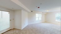 This single-floor residential unit offers a practical and functional layout designed to maximize comfort and livability. The expansive main living area is finished with neutral wall-to-wall carpeting and crisp white walls, creating a bright and versatile space filled with natural light from a large window overlooking greenery outside. Structural ceiling beams add a subtle architectural detail to the open living area.

The galley-style kitchen is efficiently laid out with warm honey-toned wood cabinetry, a white electric range, a full-size refrigerator, and a dishwasher, all set atop easy-care tile flooring. A peninsula counter connects the kitchen to the living space, providing an open, airy feel between the two areas. Conveniently located directly off the kitchen is a dedicated in-unit laundry room, housing a full-size washer and dryer along with overhead wire shelving for additional storage.

The bedroom is generously proportioned, carpeted, and features a walk-in closet as well as direct access to additional storage. The bathroom is finished with tile flooring, a vanity with wood cabinetry and a solid countertop, and connects to the main hallway. Throughout the unit, the neutral color palette, ample outlets, and HVAC venting reflect a well-maintained, move-in-ready space.