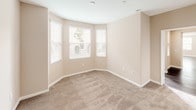 This single-story residence presents a cohesive design characterized by warm beige walls, white trim, and a combination of dark hardwood flooring and plush carpeting throughout. The spacious living area is bathed in natural light from multiple windows fitted with blinds, and dark hardwood floors extend seamlessly into the adjoining dining area, which features a pendant light fixture and direct access to an outdoor patio with views of surrounding greenery.

The kitchen is efficiently designed with white cabinetry, granite-style countertops, and stainless steel appliances including a gas range, over-the-range microwave, and dishwasher. Multiple bedrooms are finished with neutral carpet and include closets; one bedroom features a distinctive bay window configuration that enhances natural light and adds architectural interest.

The primary bathroom includes a glass-enclosed walk-in shower, dual vanities, hardwood flooring, and direct access to a walk-in closet. A secondary bathroom offers a full tub and shower combination with a grab bar. A dedicated laundry area with built-in cabinetry and access to additional storage completes the layout, offering a functional and well-organized living environment.