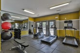 Located at 3920 Club Dr in Duluth, Georgia, this fitness center is a well-equipped, single-floor facility designed to support a well-rounded workout routine. The space immediately stands out with its bold color scheme — vibrant yellow accent walls paired with gray trim create an energetic and motivating atmosphere throughout.

The gym is outfitted with a solid selection of cardio equipment, including multiple treadmills and an elliptical trainer, as well as a stationary recumbent bike and a weight bench for strength training. A rack of dumbbells and a collection of stability and medicine balls round out the available equipment, offering users versatility in their workouts.

Durable rubber flooring covers the entire space, providing both safety and comfort underfoot. Large floor-to-ceiling mirrors line one wall, visually expanding the room and allowing users to monitor their form during exercise. The mirrors also enhance the sense of openness in the space.

Natural light filters in through multiple windows and glass-paneled doors that open to the outdoors, creating a bright and inviting environment. Overhead fluorescent lighting ensures the space remains well-lit at all hours. The layout is practical and efficiently organized, with clear circulation paths between equipment. Overall, this fitness center offers a functional and energizing environment for residents seeking convenient on-site exercise facilities.