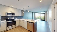 Located at 601 Bond Ave in Grand Rapids, MI, this modern one-bedroom, one-bathroom unit offers a thoughtfully designed open-concept layout with contemporary finishes throughout. Light wood-style flooring flows seamlessly across the entire space, creating a clean and cohesive aesthetic.

The combined kitchen and living area serves as the heart of the unit. The kitchen is equipped with stainless steel appliances, including a refrigerator, range, microwave, and dishwasher, complemented by white flat-panel cabinetry, a blue-grey tile backsplash, and a white quartz peninsula with an undermount sink — ideal for both cooking and casual dining. Pendant lighting adds a refined touch overhead.

The living area is bright and airy, anchored by a dramatic floor-to-ceiling glass window wall with a glass door that opens to a balcony, flooding the space with natural light and providing expansive outdoor views of the surrounding Grand Rapids landscape.

The bedroom is a comfortable, well-proportioned retreat featuring large black-framed windows that frame lush green views, paired with warm neutral walls and continuous hardwood-style flooring.

The bathroom offers a clean, modern design with large-format white tile in the tub/shower surround, a grey vanity with a white countertop, open shelving, and warm wood-tone flooring, completing this well-appointed urban residence.