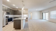 This single-story residence offers a thoughtfully designed open-concept layout that seamlessly connects the kitchen and living areas. The kitchen is a standout feature, outfitted with dark wood-grain cabinetry, granite-style countertops, a subway tile backsplash, and a full suite of stainless steel appliances including a refrigerator, electric range, over-the-range microwave, and dishwasher. A central island with pendant lighting above and a built-in desk nook nearby add both function and style. Light wood-look flooring runs throughout the kitchen, transitioning to plush neutral carpet in the spacious living area, which benefits from natural light and access to an outdoor space.

The bedrooms are generously sized, carpeted, and finished with neutral tones, providing a calm and versatile atmosphere. The primary bathroom features a soaking tub with tile surround, a granite-topped vanity with dark cabinetry, light wood-look flooring, and access to a walk-in closet with built-in shelving. A second full bathroom mirrors the same refined finishes. A dedicated laundry room houses a full-size washer and dryer with overhead shelving, completing this well-appointed home.