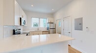 This two-floor space showcases a modern, clean design with a cohesive white-and-gold aesthetic carried throughout. The main level centers around an open-concept layout where the kitchen flows seamlessly into the living area. The kitchen is well-appointed with crisp white cabinetry, quartz countertops, a large central island, and a full suite of stainless steel appliances including a refrigerator, dishwasher, range, and microwave. Gold-toned hardware on the cabinetry adds a refined accent, and a window above the sink allows natural light to fill the space. Light wood-style flooring runs throughout the main living areas, contributing to the bright, airy atmosphere. A wall-mounted mini-split unit provides climate control on the lower level.

The upper floor features carpeted bedrooms with large windows that frame open neighborhood views, flooding each room with natural light. The bathrooms maintain the same design language as the rest of the space, featuring white quartz vanity tops, white cabinetry with gold hardware, framed mirrors, and coordinating gold towel fixtures. Louvered closet doors and recessed lighting are consistent details found throughout both floors, reinforcing the space's modern and well-finished character.