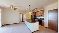 This single-floor residence is thoughtfully designed with a cohesive aesthetic defined by warm cherry wood cabinetry, dark oil-rubbed bronze hardware, and rich wood door trim that flows consistently throughout the space. Light wood flooring runs through the kitchen and hallway areas, while plush neutral carpet covers the expansive living room and bedrooms, creating a comfortable contrast in textures.

The open-concept kitchen serves as a central feature, anchored by a large island with a dark granite countertop and an undermount sink illuminated by pendant lighting. Ample cherry wood cabinetry lines the walls alongside black appliances, a stainless steel microwave, and track lighting overhead. A ceiling fan connects the kitchen to the generously sized living area, which also features a fireplace with a stone surround visible in the floor plan.

Bedrooms are bright and well-proportioned, each with ceiling fans, windows offering outdoor views, and neutral carpet. The bathrooms are finished with granite-topped vanities, cherry wood cabinetry, oil-rubbed bronze fixtures, large mirrors, and a full tub-shower combination. A dedicated in-unit laundry area accommodates a full-size washer and dryer with overhead wire shelving. Hallways connect each space with practicality and consistent design continuity.