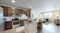 This well-appointed single-floor residence offers a thoughtfully designed open-concept layout that seamlessly connects the kitchen and living areas. The kitchen is a standout feature, showcasing rich dark-brown cabinetry, a classic white subway tile backsplash, granite countertops, and a full suite of stainless steel appliances including a range, microwave, dishwasher, and French door refrigerator. A central island with bar seating provides an ideal space for casual dining or entertaining. Wood-style flooring flows consistently throughout the unit, contributing to a cohesive and modern aesthetic. The living area is bright and welcoming, benefiting from natural light provided by large windows with blinds, and is complemented by recessed lighting and a ceiling fan overhead. A dedicated bedroom offers a clean, versatile space with its own window and views to the exterior. The bathroom features a granite-topped vanity with dark cabinetry, a tiled shower surround, and consistent wood-style flooring. Neutral wall tones throughout create a warm, inviting ambiance, while the open floor plan and recessed lighting ensure the space feels airy and functional from every angle.