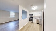 Located at 1425 N New Florissant Rd in Florissant, Missouri, this single-floor unit offers a clean, functional layout with a bright, neutral color palette throughout. The kitchen is a standout feature, outfitted with stainless steel appliances including a refrigerator, electric range, built-in microwave, and dishwasher. White shaker-style cabinetry and light granite-look countertops contribute to a fresh, contemporary aesthetic. Light hardwood-style flooring runs through the kitchen and entry areas, providing a cohesive and easy-to-maintain surface.

A distinctive architectural pass-through window connects the kitchen to the adjacent living area, enhancing the open feel of the space and allowing natural light to flow between rooms. The living area is spacious and bright, benefiting from natural light through blinds-equipped windows.

The bedroom features neutral carpeting, a ceiling fan with integrated lighting, and a window that brings in additional natural light. A walk-in closet provides convenient storage. The bathroom includes a full tub-shower combination with chrome grab bars and a clean white surround. A dedicated entry area with a coat closet adds further practical storage to this well-designed unit.