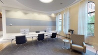 This refined office space masterfully combines classical architectural heritage with contemporary design sensibilities. The most striking architectural feature is the sweeping curved ceiling with a recessed circular detail, lending the room a sense of grandeur and visual depth. Soft, diffused overhead lighting complements the smooth, pale tones of the ceiling and walls, creating a bright and focused work environment.

The workstation area is arranged along a sleek, minimalist white desk with multiple computer monitors and ergonomic modern chairs with polished chrome bases, reflecting a professional and functional layout. Textured wall panels in soft grey tones add dimension and acoustic quality to the space, while neutral grey carpeting grounds the room with a quiet, sophisticated feel.

Large arched windows — a nod to the building's classical origins — are dressed with sheer white curtains that diffuse natural light gracefully throughout the room. A comfortable seating area with a silver accent chair and a glass side table provides a more relaxed setting within the workspace. Additional office equipment, including a multi-function printer, is neatly integrated into the layout. The overall ambiance is polished, calm, and highly professional, ideal for a focused and elegant working environment.