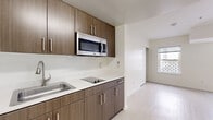 Located at 302 Arizona Ave in the heart of Santa Monica, California, this one-bedroom, one-bathroom residence offers a thoughtfully designed single-floor layout that maximizes every inch of its compact footprint. Light-toned wood-style flooring runs throughout, lending a clean, contemporary feel to the entire space.

The kitchen is a functional highlight, outfitted with rich dark-wood grain cabinetry — both upper and lower — paired with crisp white countertops that create a striking visual contrast. A stainless steel sink, built-in electric cooktop, and over-the-range microwave provide all essential cooking amenities in a streamlined, efficient arrangement.

The bedroom is a well-proportioned retreat with bright white walls, light flooring, and natural light filtering in through a window. Its clean, open design allows for flexible furniture arrangements. A dedicated walk-in closet adjacent to the bedroom features built-in shelving and hanging rod, offering practical storage solutions.

The bathroom includes a full-size soaking tub and shower combination, accented by a distinctive green tile border, a wall-mounted sink, and a mirrored vanity — all presented in a clean, utilitarian style. The overall ambiance of the residence is modern and minimalist, well-suited for urban living steps from the shops, dining, and beaches of Santa Monica.