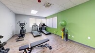 Located at 1930 Marion St in Columbia, South Carolina, this dedicated exercise room offers a well-equipped fitness space designed to support a variety of workout routines. The room features a drop ceiling with recessed panel lighting and skylights that provide bright, even illumination throughout. Natural light also filters in through multiple windows dressed with horizontal blinds, adding an open feel to the space.

The flooring throughout is a warm, light-toned hardwood-style surface that is both practical and easy to maintain. The walls are painted in energizing accent colors — vibrant lime green and bold yellow — that create a motivating atmosphere ideal for physical activity.

The space is thoughtfully organized with distinct workout zones. A cardio area along one wall houses two treadmills and an elliptical machine, positioned near windows for a pleasant exercise environment. A strength training zone includes a multi-function cable machine, an adjustable weight bench, and a full dumbbell rack with a wide range of weights. A functional training area features a stability ball, resistance bands, and other accessory equipment neatly stored on a vertical storage stand. A sliding barn-style door provides access, adding a modern architectural detail. Climate control is handled by a ceiling-mounted HVAC unit, ensuring year-round comfort during workouts.