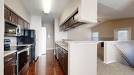 This two-floor residence offers a well-organized layout with a blend of hardwood-style flooring and plush carpet across its living spaces. The galley-style kitchen is a standout feature, equipped with dark espresso cabinetry, granite-look countertops, stainless steel appliances including a built-in microwave and range, a black refrigerator, and an undermount sink. Upper and lower cabinetry provide ample storage, while a peninsula counter creates a natural transition into the adjoining living area. The living room is bright and airy, highlighted by soaring vaulted ceilings, a ceiling fan, and an open-concept connection to the kitchen. Neutral carpet and warm-toned walls contribute to a comfortable, inviting ambiance. The bathroom features rich hardwood-style flooring, dark cabinetry with a granite-look vanity top, a tub-shower combination with tiled surround, and direct access to a spacious walk-in closet with built-in shelving. The bedrooms are carpeted, well-lit by natural light through slatted windows, and offer generous proportions. A dedicated laundry room includes washer and dryer hookups with both electric and gas connections. Throughout, the consistent use of dark hardware and neutral tones creates a cohesive and modern aesthetic.