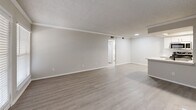 Located at 4753 Old Bent Tree Lane in Dallas, TX, this 1-bedroom, 2-bathroom unit offers a well-designed single-floor layout with a clean, modern aesthetic throughout. Light wood-look flooring flows seamlessly across the living areas, complementing the neutral gray walls and white trim that give the space a bright, cohesive feel.

The open living room is accented by crown molding, a textured ceiling, and a ceiling fan, with a front door and adjacent window allowing natural light to fill the space. A fireplace serves as a focal point, adding warmth to the living area.

The kitchen is a standout feature, offering a galley-style layout with white shaker cabinetry, light quartz countertops, a peninsula with a stainless steel sink and matte black faucet, and a full suite of stainless steel appliances including a range, microwave, refrigerator, and dishwasher. Built-in open shelving adds functional character.

The bedroom is a comfortable size, featuring light wood-look flooring, a ceiling fan, a window with natural light, and easy access to a dedicated closet. Both bathrooms are well-appointed with white cabinetry, quartz countertops, matte black fixtures, large mirrors, and tub-shower combinations with white tile surrounds.