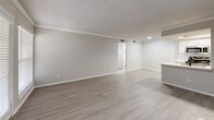 Located at 4753 Old Bent Tree Lane in Dallas, TX, this 1-bedroom, 2-bathroom unit offers a well-designed single-floor layout with a clean, modern aesthetic throughout. Light wood-look flooring flows seamlessly across the living areas, complementing the neutral gray walls and white trim that give the space a bright, cohesive feel.

The open living room is accented by crown molding, a textured ceiling, and a ceiling fan, with a front door and adjacent window allowing natural light to fill the space. A fireplace serves as a focal point, adding warmth to the living area.

The kitchen is a standout feature, offering a galley-style layout with white shaker cabinetry, light quartz countertops, a peninsula with a stainless steel sink and matte black faucet, and a full suite of stainless steel appliances including a range, microwave, refrigerator, and dishwasher. Built-in open shelving adds functional character.

The bedroom is a comfortable size, featuring light wood-look flooring, a ceiling fan, a window with natural light, and easy access to a dedicated closet. Both bathrooms are well-appointed with white cabinetry, quartz countertops, matte black fixtures, large mirrors, and tub-shower combinations with white tile surrounds.